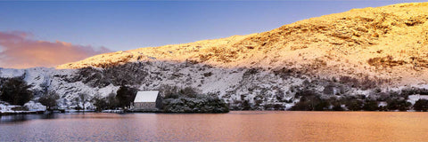 Dawn light turning snow pink at Gougane Barra with mountains reflected in the still lake, Cork