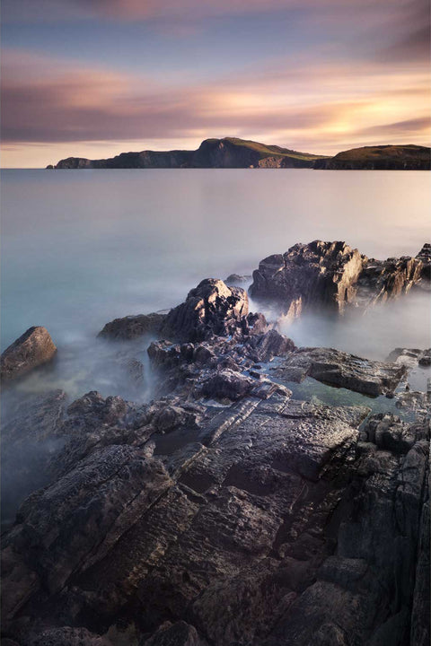 Long exposure sunset view of Toe Head on Cork's south coast with foreground rocks leading to the imposing headland