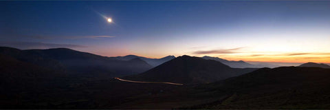 Car headlight trails curving through the Glantrasna Valley at twilight with the Beara Mountains silhouetted against the fading sky