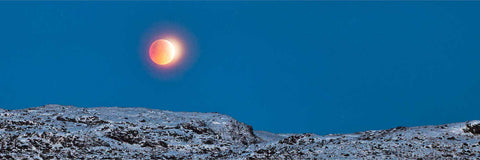 Total lunar eclipse glowing red above snow-covered mountains at Gougane Barra, Cork, on the winter solstice