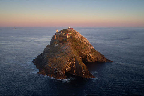 Aerial view of Bull Rock island at sunrise showing the lighthouse, natural tunnel, and buildings, Cork