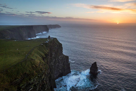 Aerial view of O'Brien's Tower on the Cliffs of Moher bathed in warm sunset light with the Atlantic Ocean reflecting golden hues