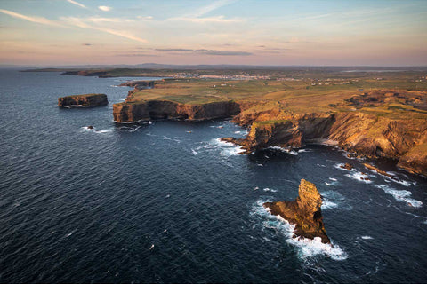 Golden light over the rugged cliffs and gentle waves at Kilkee on the Clare coastline at sunset
