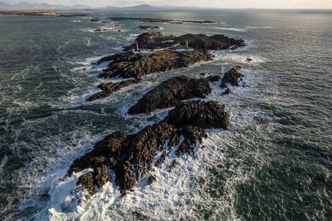 Aerial view of Slyne Head twin lighthouses on rocky outcrops with Atlantic waves crashing around them, Galway