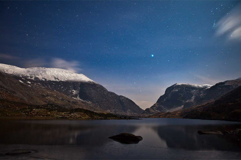 Moonlit winter night in the Gap of Dunloe, Kerry with snow-covered mountains and a still lake reflecting the sky