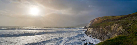 Stormy Atlantic waves crashing against jagged rocks at Slea Head with sunlight breaking through clouds, Kerry