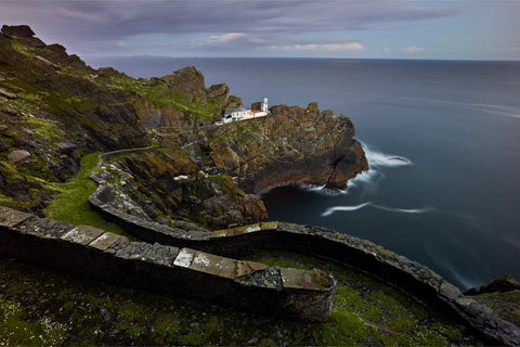 Skellig Michael lower lighthouse illuminated by moonrise with winding road descending through rocky island terrain at night