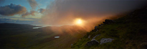 Dramatic sunrise over the Conor Pass in Dingle with sunlight filtering through layers of mountain mist and low cloud