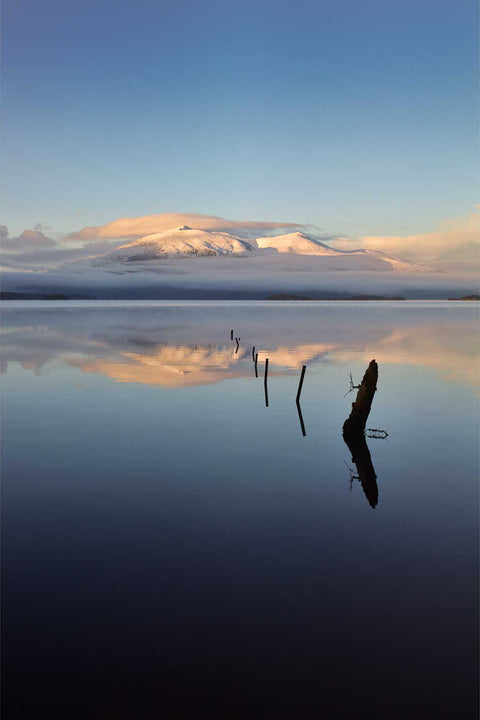 Snow-capped Purple Mountain group emerging from fog above the mirror-still waters of Lough Leane, Killarney