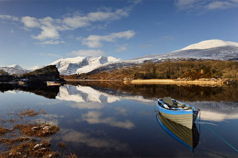 A boat moored on Upper Lake, Killarney, with snow-capped MacGillycuddy's Reeks reflected in the still water