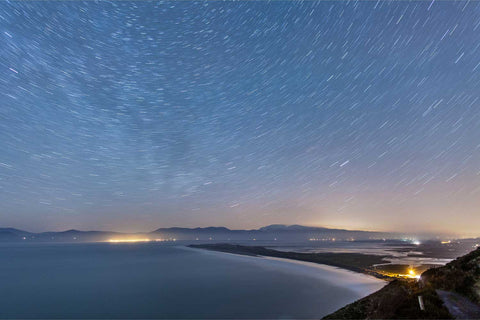Star trails over Rossbeigh Strand on a winter night with snow-capped Brandon Mountain visible on the horizon across Dingle Bay