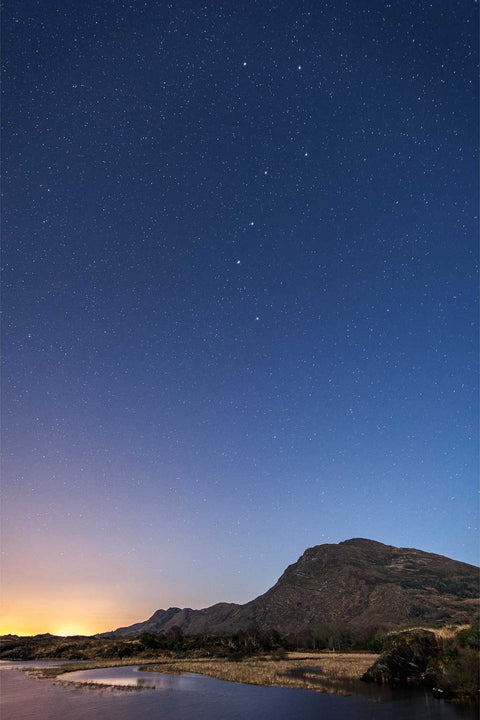 Night sky over Torc Mountain in Killarney with the Plough constellation and town glow reflected in still lake water