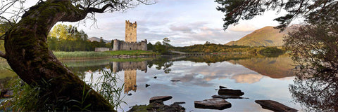 Panoramic view of Ross Castle reflected in the calm waters of Lough Leane on a summer morning in Killarney with mountains behind