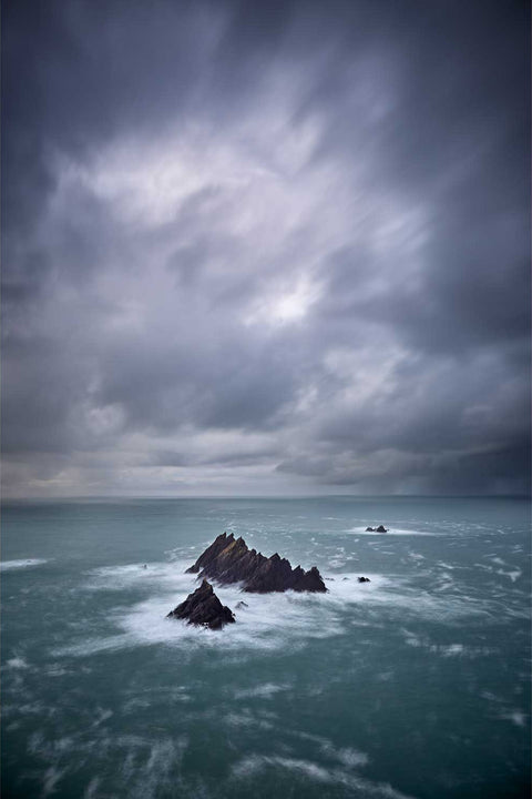Jagged Tiaracht Rocks rising from turbulent Atlantic waters under moody skies at Ireland's westernmost point