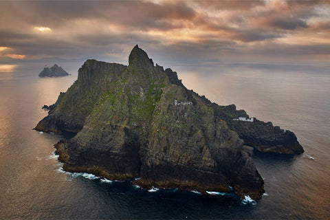 Skellig Michael at sunrise showing both lighthouses with shafts of sunlight breaking through brooding clouds over the Atlantic