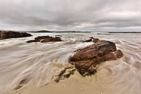 Incoming tide flowing around rocks at Silver Strand beach at the base of Mweelrea Mountain, County Mayo