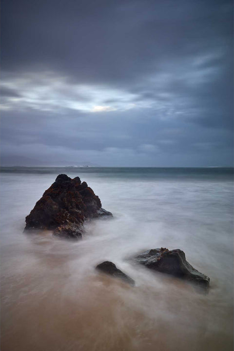 Rock outcrop standing against the incoming tide at Keem Beach, surrounded by dramatic cliffs on Achill Island, Mayo