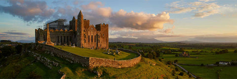 Aerial panoramic view of the Rock of Cashel at sunset, medieval towers glowing on a limestone outcrop in Tipperary