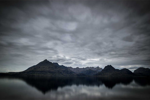 The Black Cuillin ridge reflected in perfectly still water at Elgol on the Isle of Skye under a brooding overcast sky