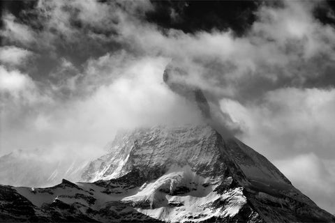 The Matterhorn in black and white, snow-covered peak half-consumed by swirling cloud with dramatic light on the upper slopes