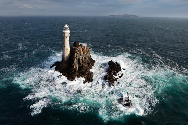 The Fastnet Rock from the air, the lighthouse low at the seaward edge with surf all around