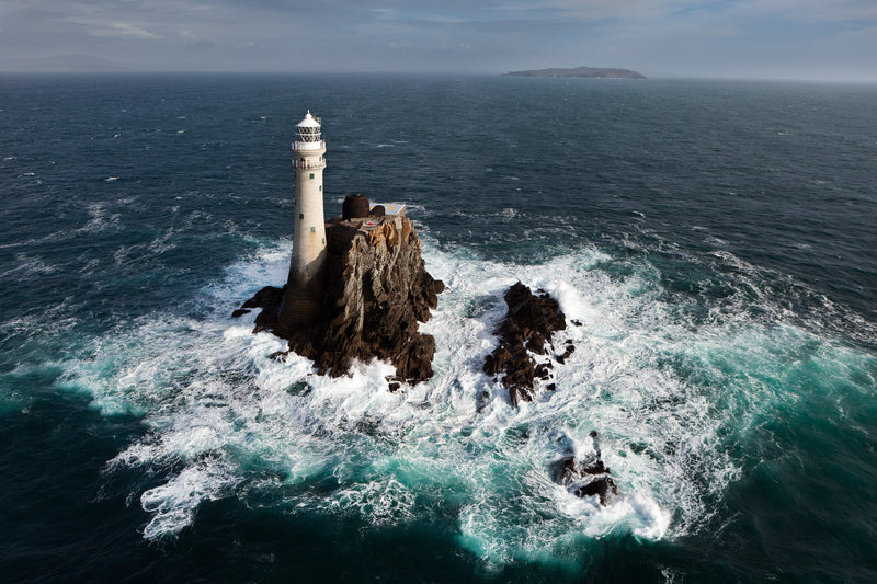The Fastnet Rock from the air, the lighthouse low at the seaward edge with surf all around