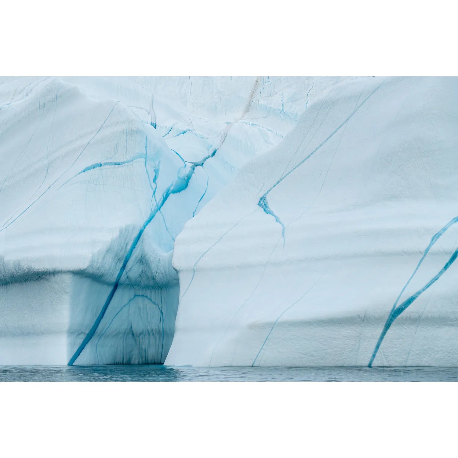 Blue veins branching across the pale surface of an iceberg above the Arctic sea in Scoresby Sound, Greenland, fine art landscape photograph by Peter Cox