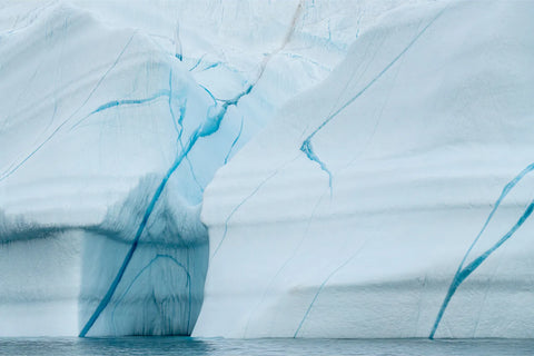Blue veins branching across the pale surface of an iceberg above the Arctic sea in Scoresby Sound, Greenland, fine art landscape photograph by Peter Cox