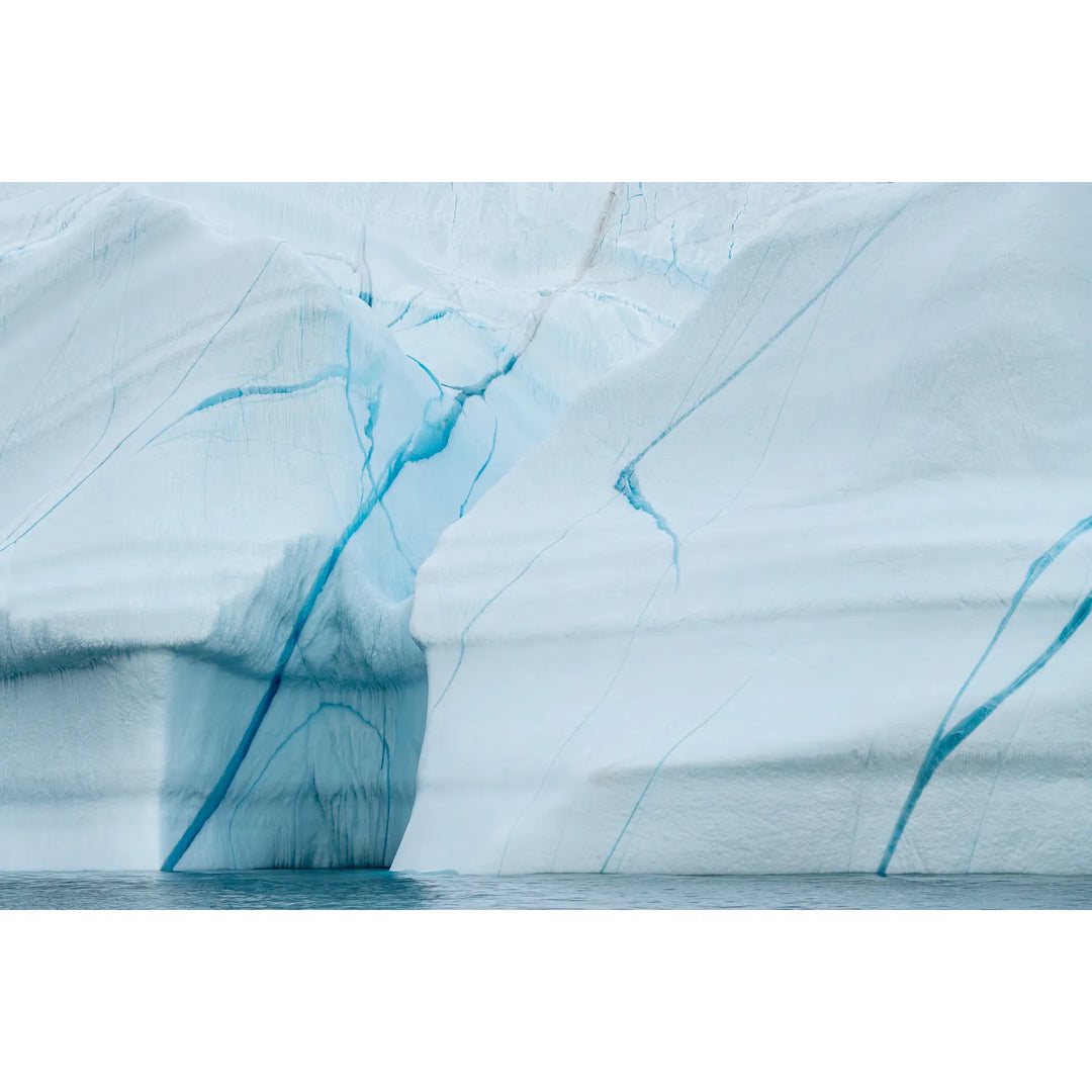 Blue veins branching across the pale surface of an iceberg above the Arctic sea in Scoresby Sound, Greenland, fine art landscape photograph by Peter Cox