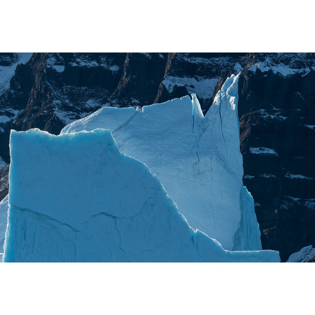 Massive blue iceberg with jagged peaks against snowy mountains, Scoresby Sound, Greenland — fine art landscape photograph by Peter Cox