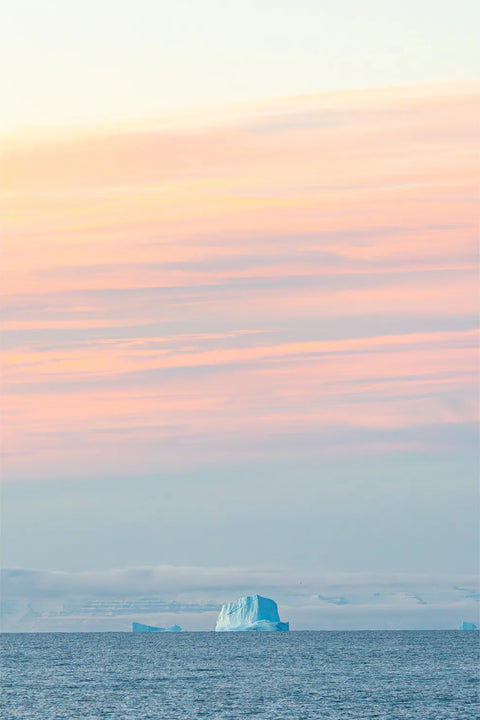 A lone blue iceberg on the horizon beneath a pastel dawn sky at Scoresby Sound, Greenland — fine art landscape photograph by Peter Cox