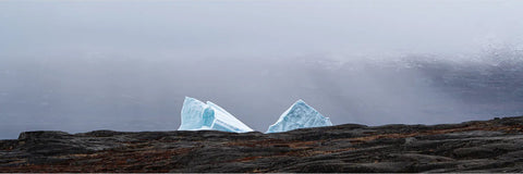 Two pale blue iceberg peaks rising above a dark Arctic ridge in fog at Scoresby Sound, Greenland