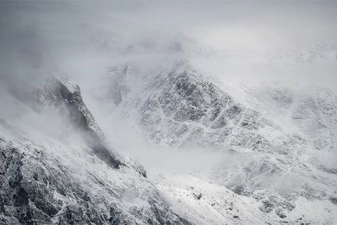 Snow-covered mountain peaks emerging through storm clouds in Scoresby Sound, Greenland — fine art landscape photograph by Peter Cox