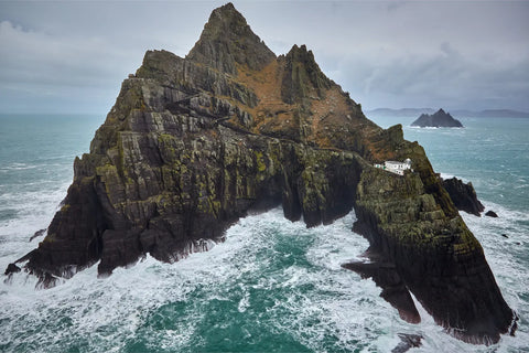 Aerial drone view of Skellig Michael's jagged cliffs battered by stormy Atlantic waves with teal-green sea and Little Skellig behind, Kerry